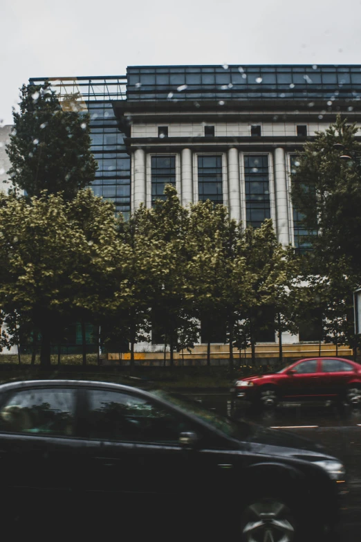 a black car driving down a street next to a tall building, unsplash, vancouver school, giant cherry trees, low quality photo, germany. wide shot, multiple stories