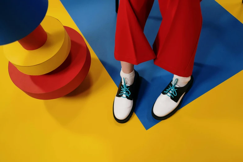 a person standing on top of a blue and yellow floor, inspired by Bauhaus, trending on pexels, de stijl, red shoes, white and teal metallic accents, avatar image, black+velvet+red+turquoise