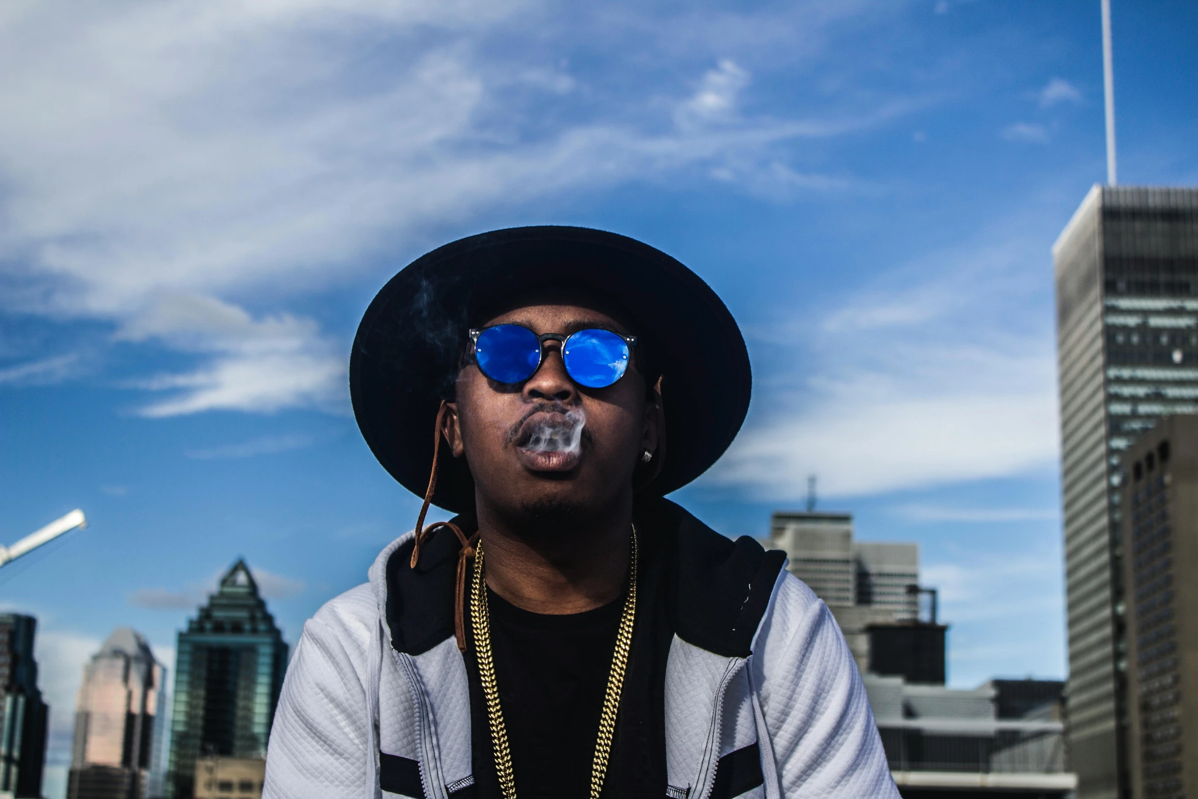 a man in a hat and sunglasses smoking a cigarette, an album cover, unsplash, african canadian, high rises, shot in the sky, big floppa