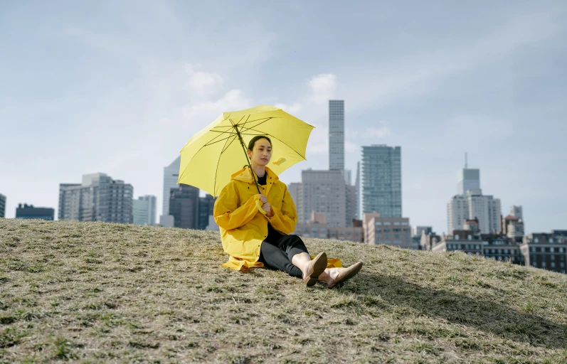 a woman sitting on a hill holding a yellow umbrella, katherine lam, **cinematic, humans of new york, a portrait of issey miyake