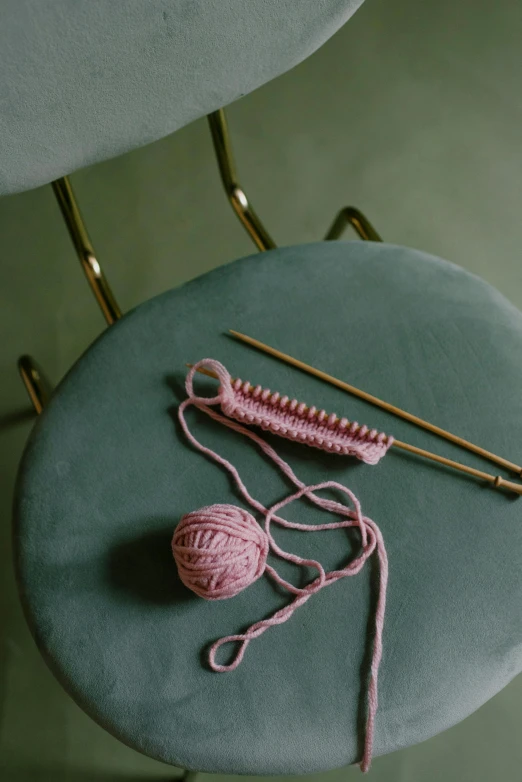 a table with a ball of yarn and knitting needles on it, a picture, inspired by Caro Niederer, trending on pexels, pink and gold, made of wool, single chair brass, high quality image