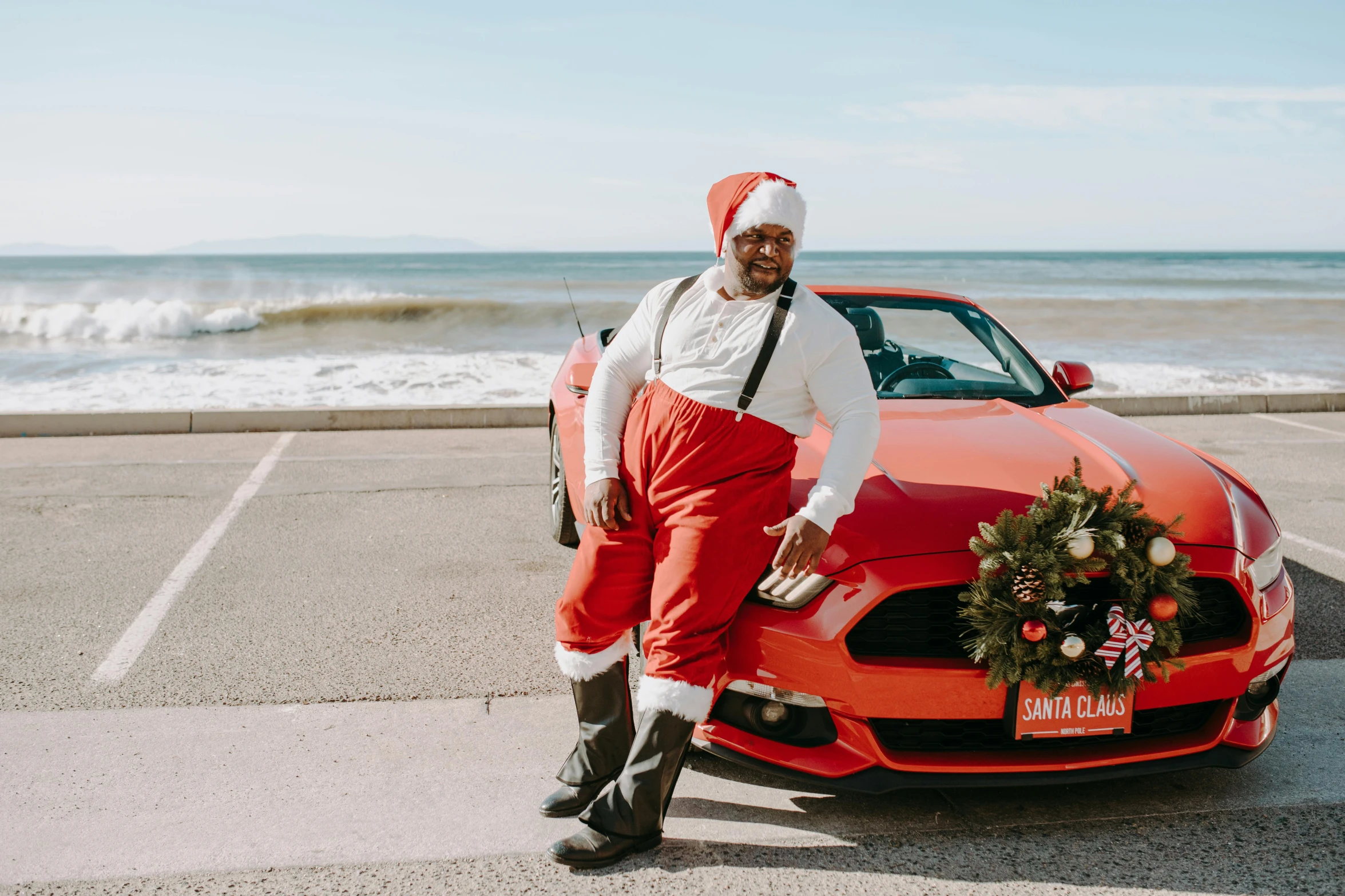 a man standing next to a red sports car, by Carey Morris, pexels contest winner, sitting on santa, lizzo, coastal, mustang