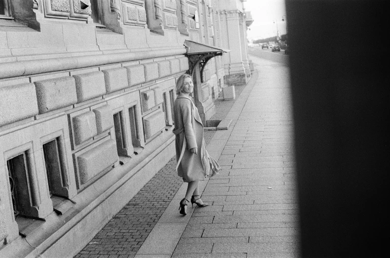 a black and white photo of a woman walking down a sidewalk, inspired by Henri Cartier-Bresson, unsplash, helsinki, tri - x pan stock, blonde woman, at the seaside