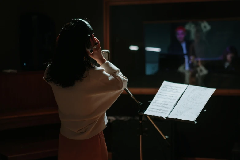 a woman that is standing in front of a microphone, an album cover, by Julia Pishtar, pexels, behind the scenes photo, [ cinematic, performing, orchestra