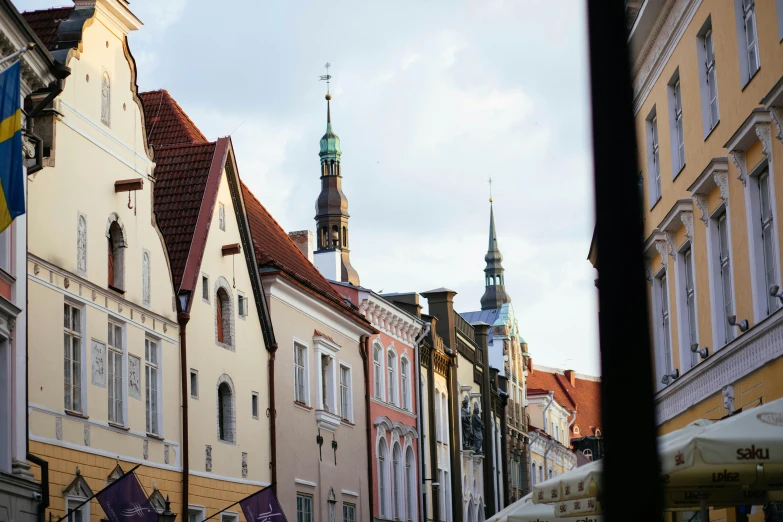 a group of people walking down a street next to tall buildings, a photo, by Julia Pishtar, pexels contest winner, baroque, capital of estonia, purple roofs, old shops, looking from slightly below