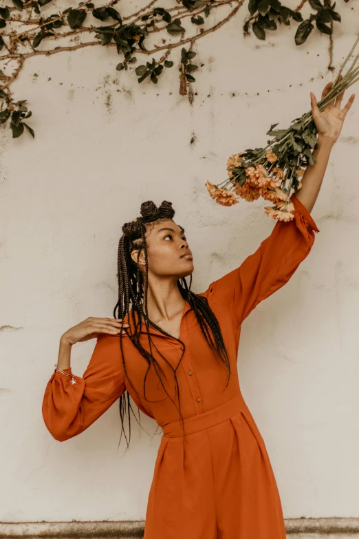 a woman in an orange jumpsuit holding a bunch of flowers, by Dulah Marie Evans, pexels contest winner, renaissance, long dreadlocks, in front of white back drop, young woman looking up, with a ponytail