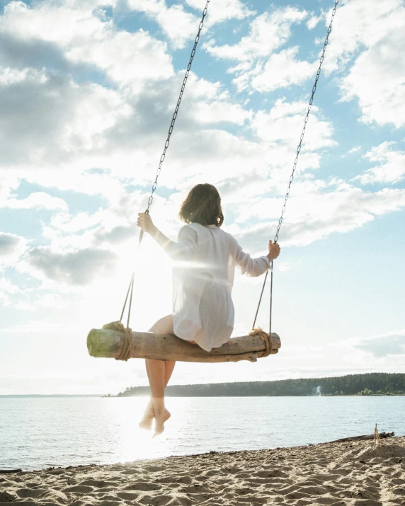 a woman sitting on a swing on the beach, inspired by Wilhelm Hammershøi, pexels contest winner, lgbtq, sitting on a log, al fresco, soaring