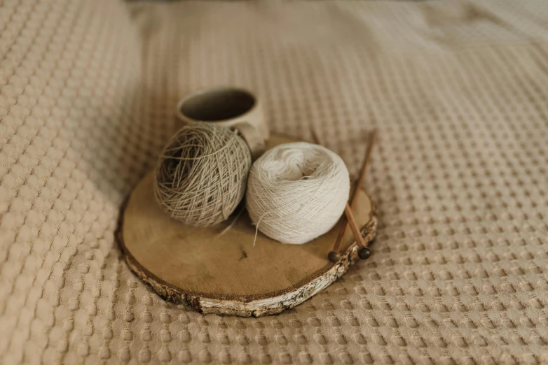 two balls of yarn sitting on a piece of wood, trending on pexels, arts and crafts movement, beige, on a wooden tray, miniature product photo, silver，ivory