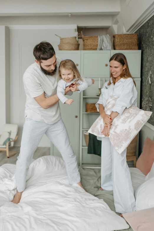 a man and woman playing with a child on a bed, pexels contest winner, happening, standing, wearing white pajamas, promo image, dancing with each other