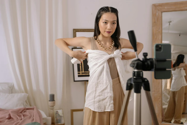 a woman that is standing in front of a camera, inspired by helen huang, trending on pexels, white sarong, wearing a vest top, tied - up shirt, leslie zhang