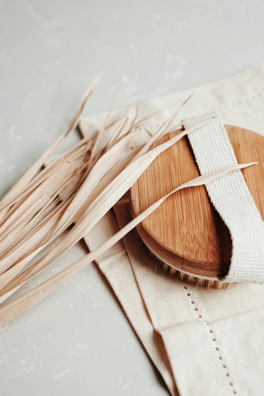 a wooden brush sitting on top of a white cloth, fronds, cloth wraps, sleek round shapes, textured base ; product photos