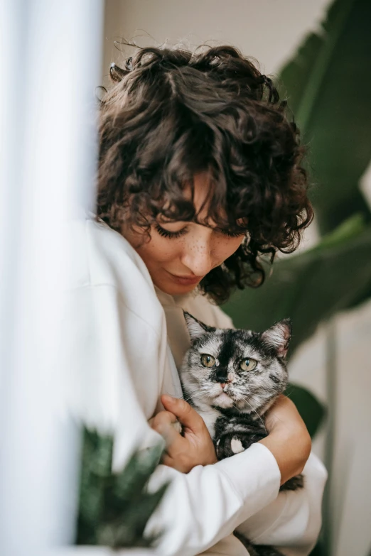 a woman holding a cat in her arms, by Julia Pishtar, trending on pexels, brown curly hair, wearing a grey robe, tuxedo cat, silver curly hair