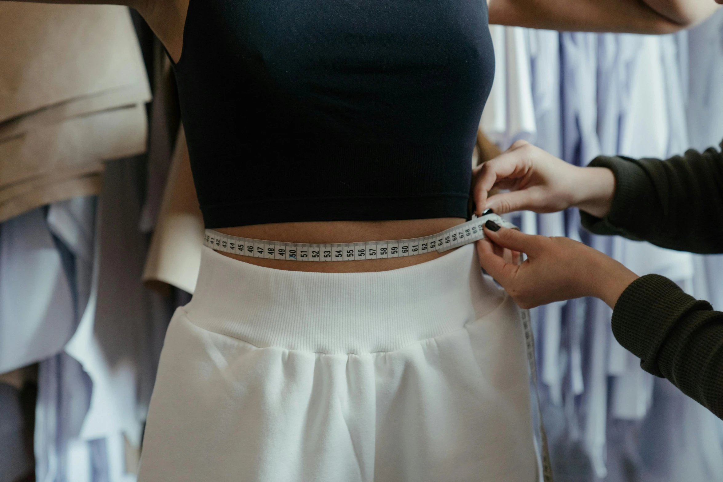 a woman measuring her waist with a measuring tape, by Emma Andijewska, trending on pexels, wearing white skirt, white and black clothing, wearing fantasy formal clothing, wearing a baggy