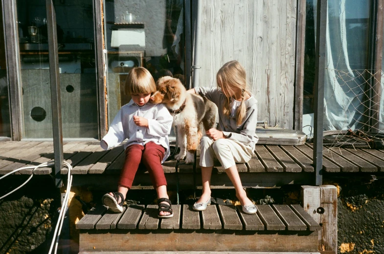 two children sitting on a porch with a dog, by Nina Hamnett, pexels contest winner, at the waterside, blonde, on a wooden table, brown