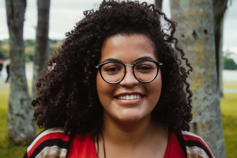 a woman with glasses smiling at the camera, by Carey Morris, pexels contest winner, mixed race, curls, avatar image, 18 years old