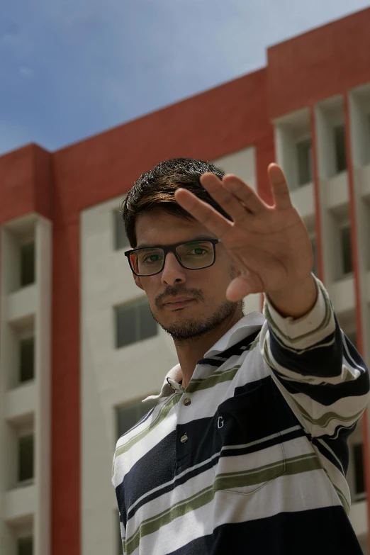 a man that is standing in front of a building, by Rajesh Soni, wave a hand at the camera, jewish young man with glasses, **cinematic, fzd school of design
