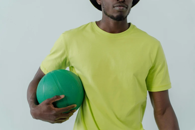 a man in a yellow shirt holding a green ball, inspired by Paul Georges, trending on pexels, baggy clothing and hat, ( ( dark skin ) ), no logo, local gym