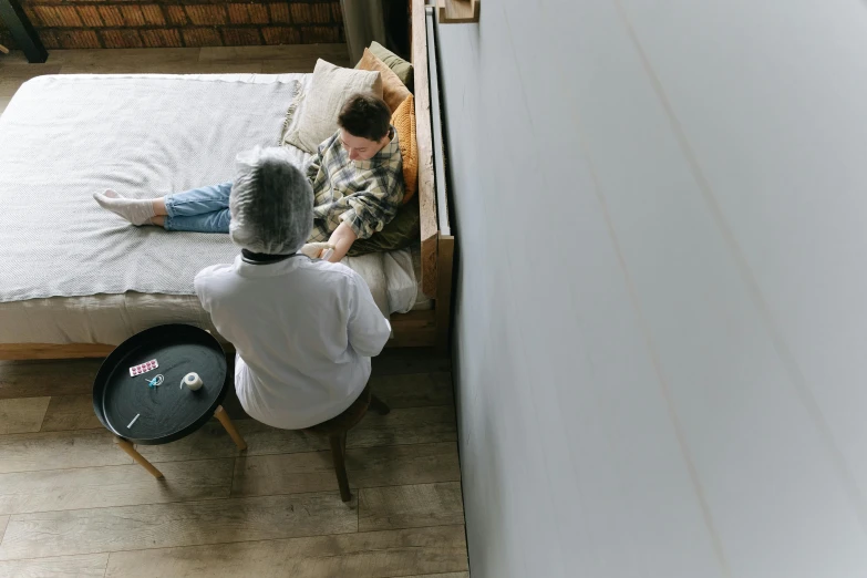 a man sitting on top of a bed next to a woman, by Emma Andijewska, pexels contest winner, wolfy nail, healthcare worker, sitting on a mocha-colored table, grey