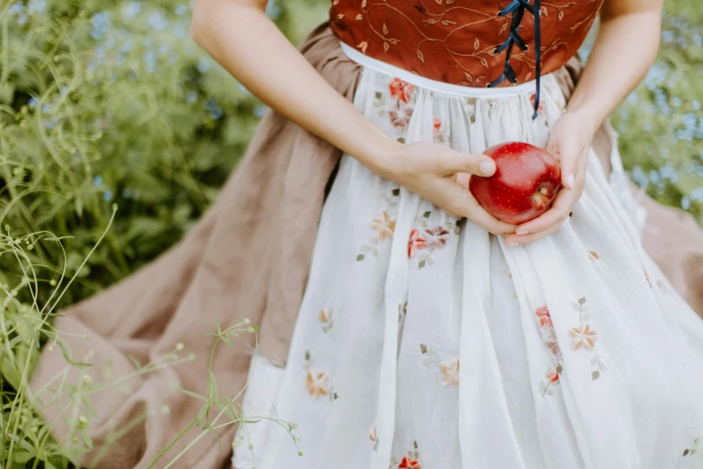 a woman in a dress holding an apple, inspired by Elsa Beskow, pexels contest winner, renaissance, red and white color theme, organic dress, layered skirts, girl of the alps