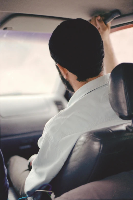 a man sitting in the passenger seat of a car, unsplash, muslim, wearing a white shirt, back of head, square