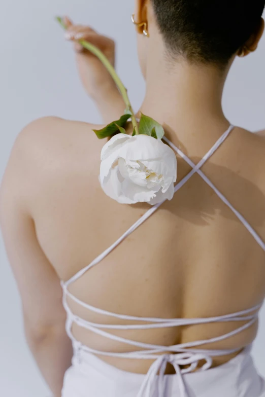 a woman with a flower in her hair, inspired by Ren Hang, unsplash, renaissance, showing her shoulder from back, bra strap, white human spine, holding a rose