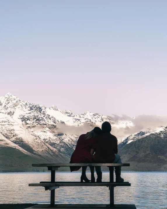 a couple of people that are sitting on a bench, by Sophie Pemberton, pexels contest winner, majestic snowy mountains, lesbians, in lake, new zeeland