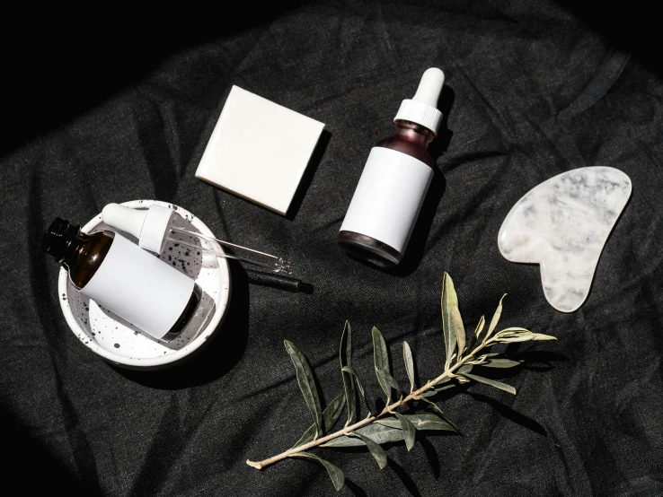 an assortment of skin care products laid out on a black cloth, a black and white photo, by Emma Andijewska, trending on pexels, eucalyptus, objects levitating, white clay, oils