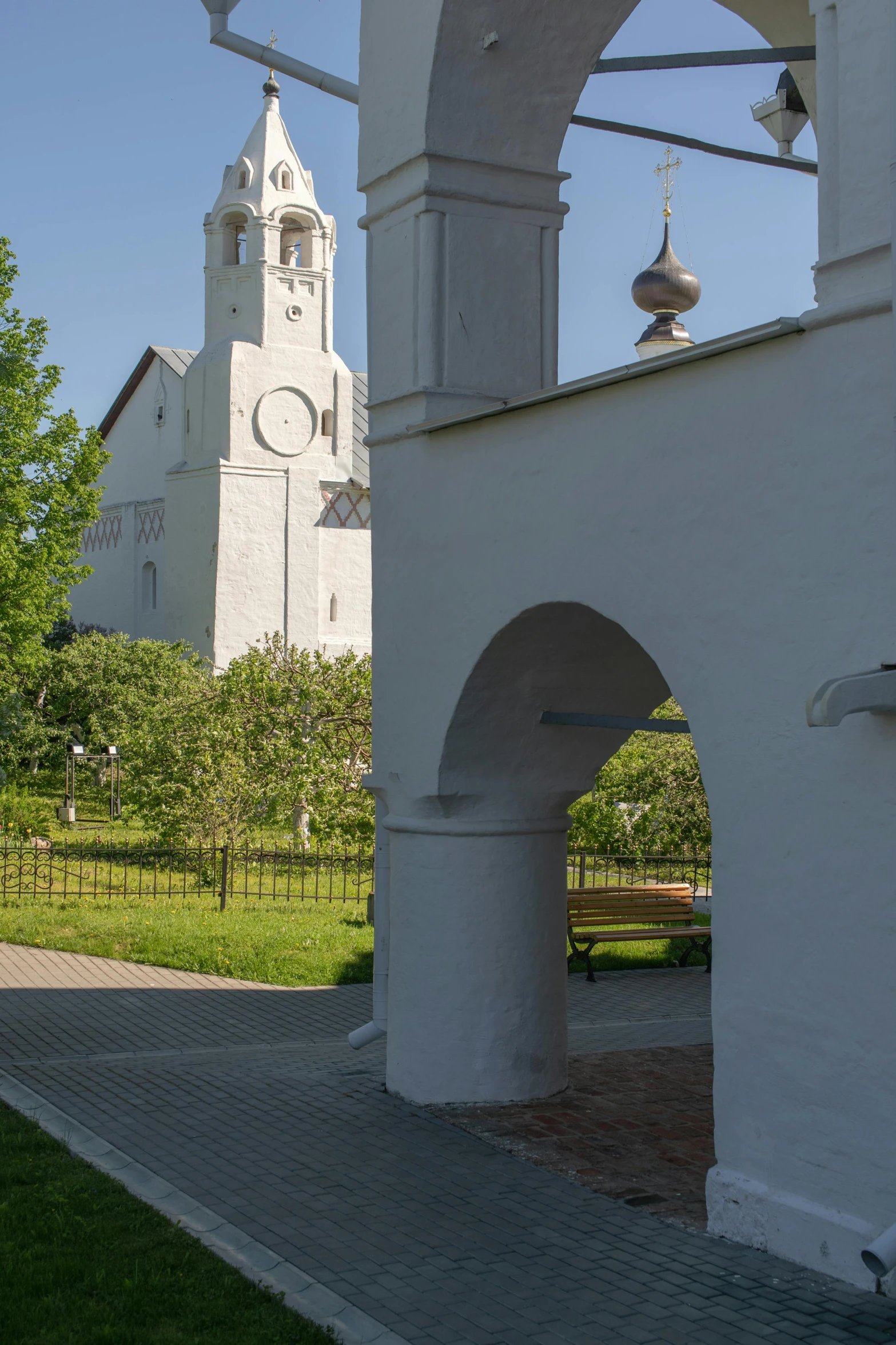 a clock that is on the side of a building, a picture, inspired by Illarion Pryanishnikov, romanesque, white sweeping arches, shadow of catholic church cross, parks and gardens, tarmo juhola