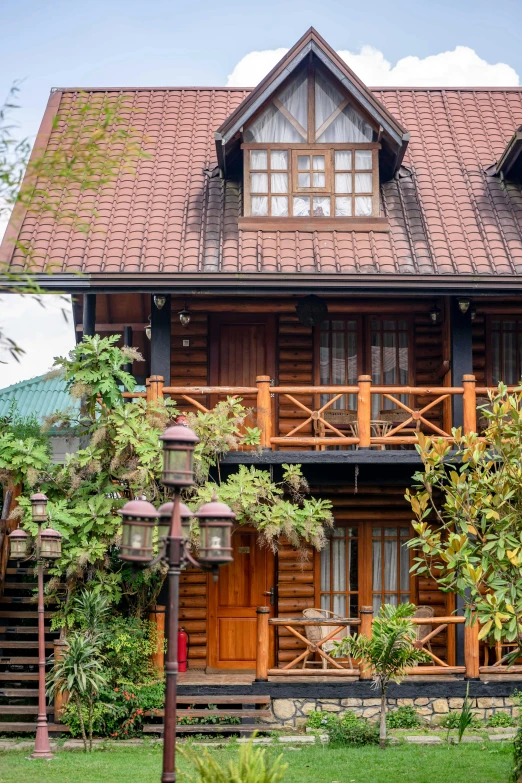 a large wooden house sitting on top of a lush green field, plants on balconies, hanging lanterns, 2019 trending photo, chalet