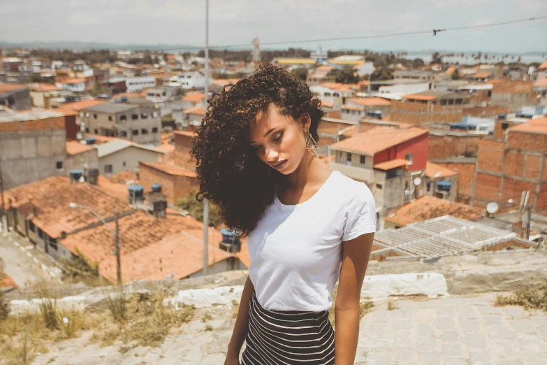 a beautiful young woman standing on top of a building, pexels contest winner, (dark shorter curly hair), brazilan supermodel, ( ( brown skin ) ), mixed-race woman