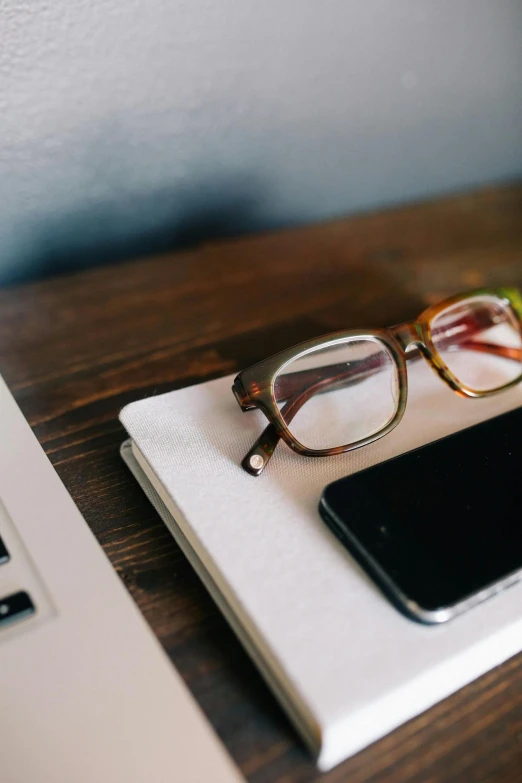 an open laptop computer sitting on top of a wooden desk, by Carey Morris, trending on pexels, square rimmed glasses, corporate phone app icon, brown, a small