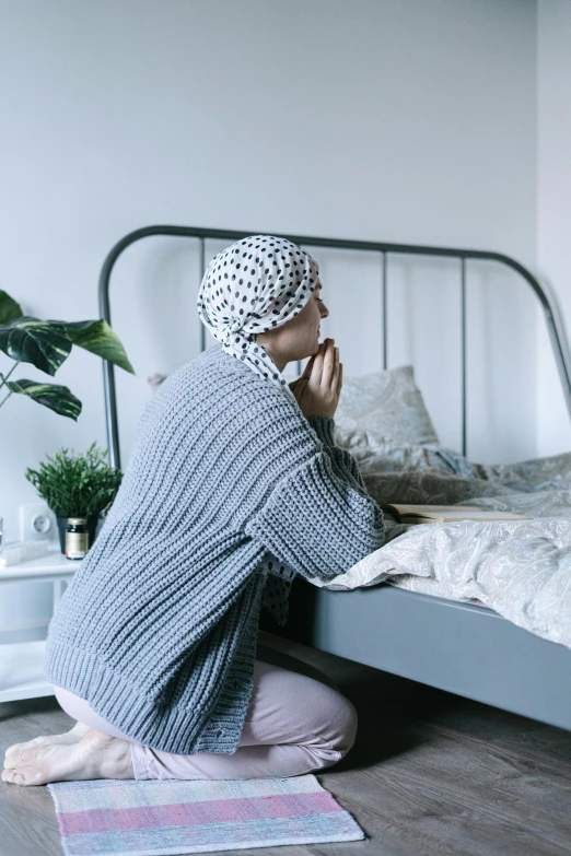 a woman sitting on a bed talking on a cell phone, pexels, hurufiyya, praying, wearing a head scarf, with a bunk bed, head bowed slightly