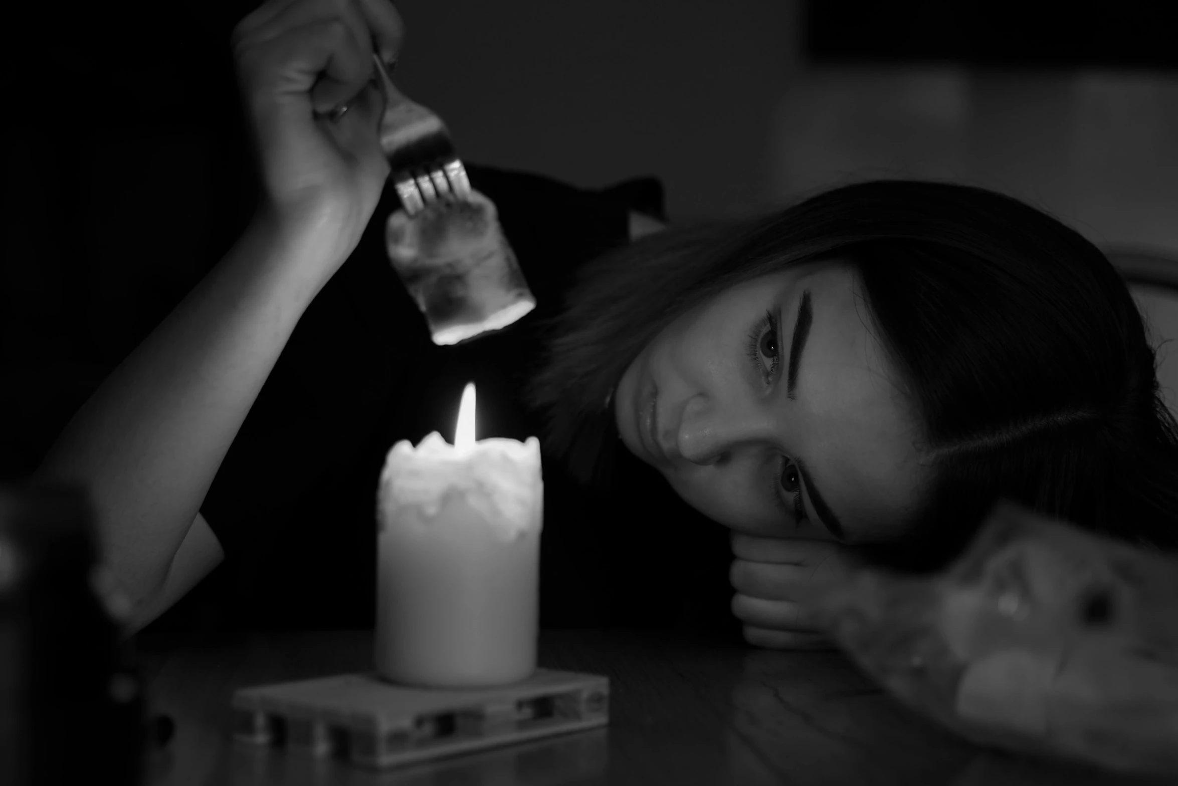 a woman laying on top of a table next to a candle, a black and white photo, by Adam Marczyński, pexels contest winner, holding a candle, sadness look, dim flashlight lighting, profile picture