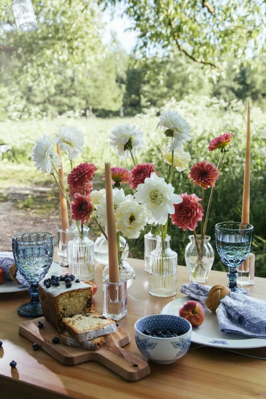 a wooden table topped with plates of food and flowers, summer field, muted blue and red tones, blown glass, dwell