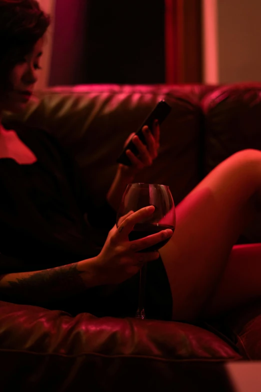 a woman sitting on a couch holding a glass of wine, inspired by Nan Goldin, trending on pexels, happening, cyberpunk strip clubs, looking at his phone, lesbians, crimson themed