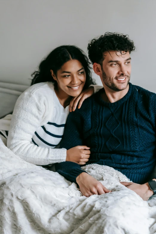 a man and a woman sitting on a bed, trending on pexels, wearing a sweater, holding each other, indigo, proud looking