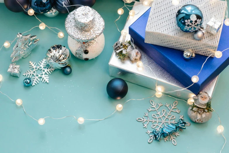a pile of presents sitting on top of a table, a still life, trending on pexels, blue and silver, string lights, turquoise color scheme, snowflakes