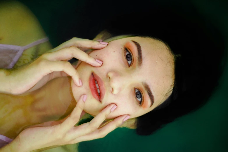 a woman posing for a picture with her hands on her face, inspired by Elsa Bleda, trending on pexels, hyperrealism, underwater face, skincare, high angle closeup portrait, green colored skin