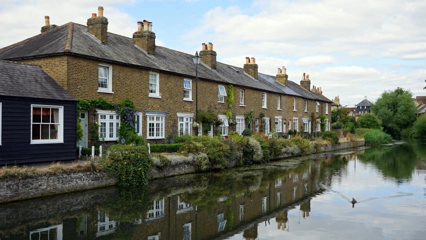 a row of houses next to a body of water, by Carey Morris, shutterstock, arts and crafts movement, blocked drains, regeneration, golden windows, cottagecore!!