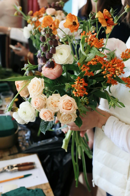 a woman holding a bunch of flowers in her hands, a still life, featured on instagram, white and orange, creating a soft, floral design, commercially ready