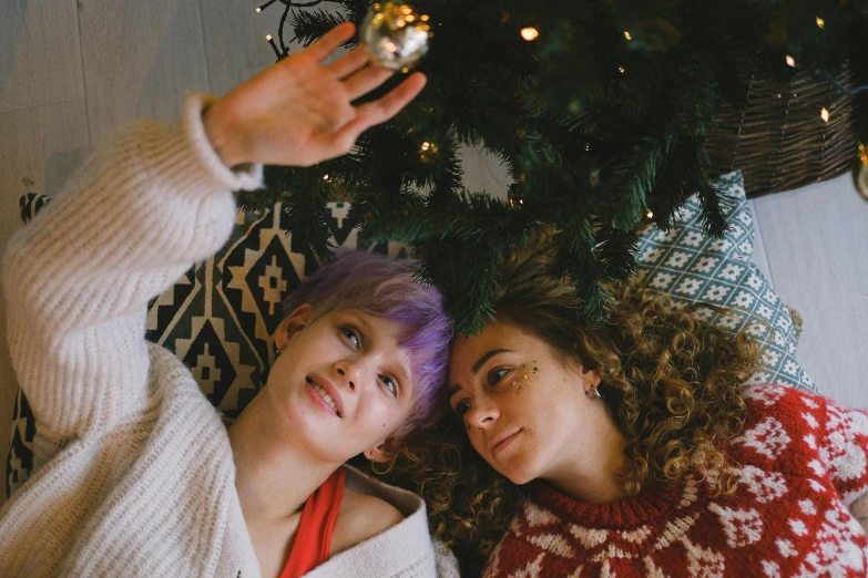 a couple of women laying next to a christmas tree, a photo, trending on pexels, lilac hair, full pov, hanging, lesbian