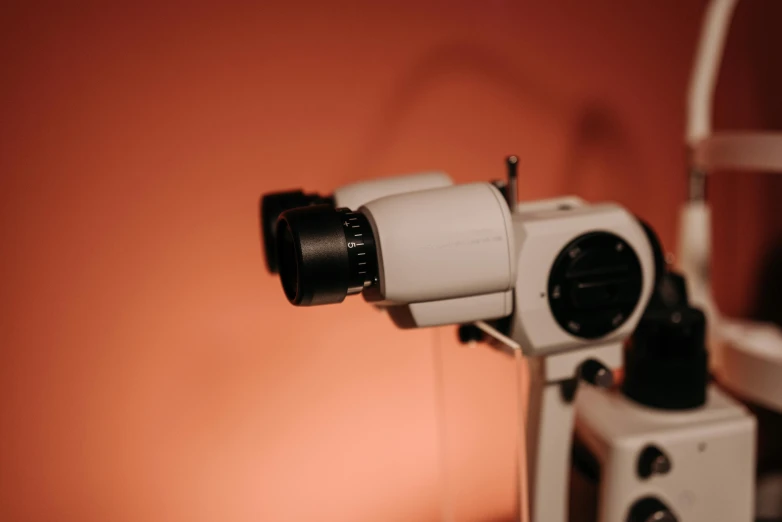 a close up of a microscope on a table, by Carey Morris, trending on pexels, photorealism, in front of an orange background, detailed : cornea, close up camera angle, surgical equipment