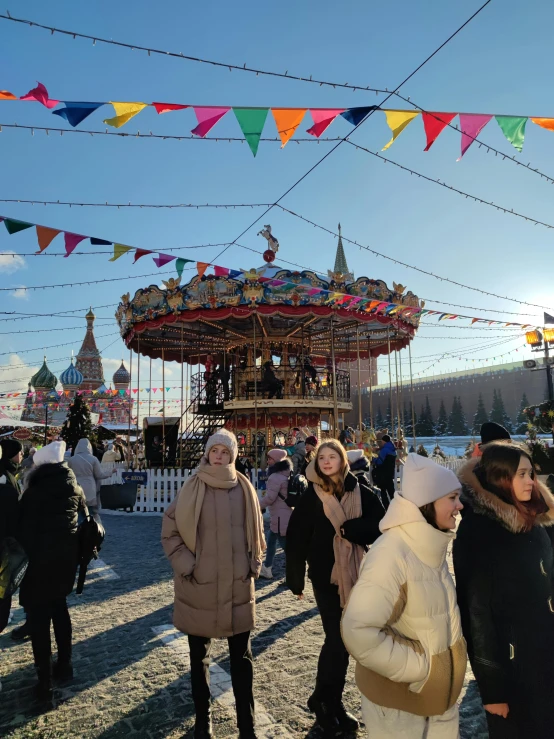 a group of people standing in front of a carousel, red square, cold as ice! 🧊, sunny environment, holiday season