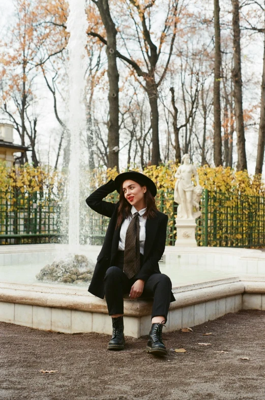 a woman sitting in front of a fountain, a portrait, trending on unsplash, baroque, a suited man in a hat, ukraine. professional photo, wearing black boots, in style of valentin serov