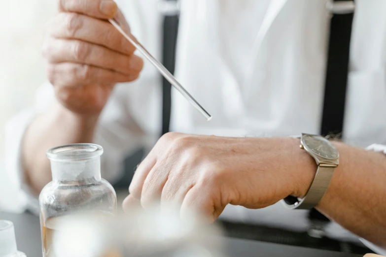 a man sitting at a table with a spoon in his hand, trending on pexels, glass vials, white lab coat, wearing a watch, holding a staff
