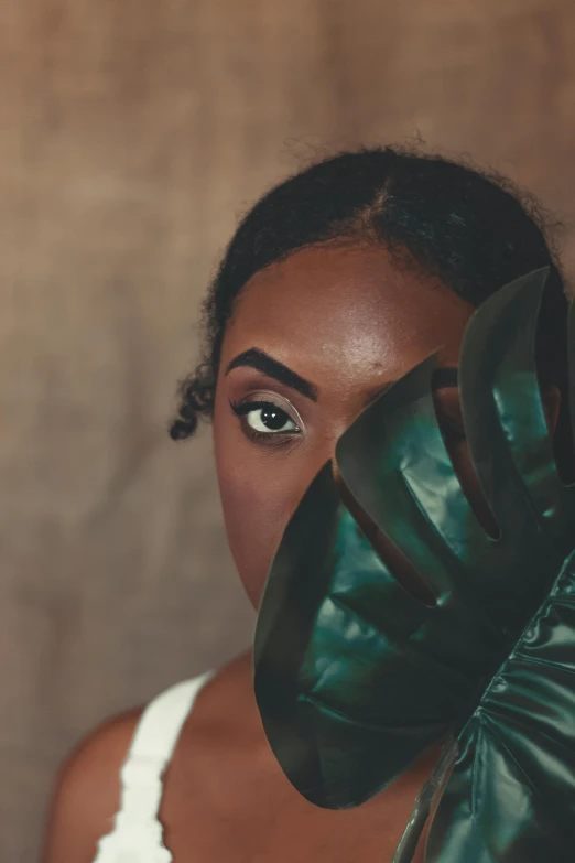 a woman holding a large leaf in front of her face, inspired by Gordon Parks, trending on pexels, afrofuturism, wearing vibrant boxing gloves, with deep green eyes, porcelain skin ”, black young woman