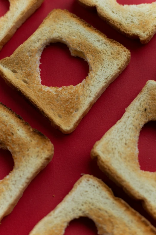 a red table topped with slices of bread, trending on pexels, romanticism, heart shaped face, squares, toast, cheerios