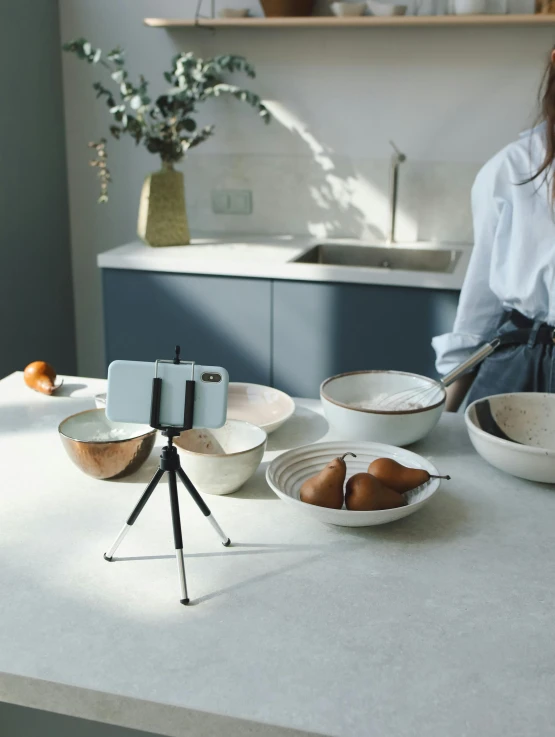 a woman standing in a kitchen preparing food, inspired by Sarah Lucas, unsplash, video art, tripod, hold up smartphone, macro lens product photo, stand on stone floor