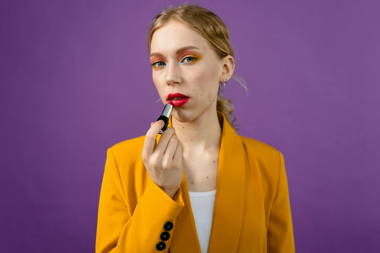 a woman is putting lipstick on her lips, by Julia Pishtar, trending on pexels, pop art, yellow purple, wearing a black and red suit, miniature product photo, portrait sophie mudd