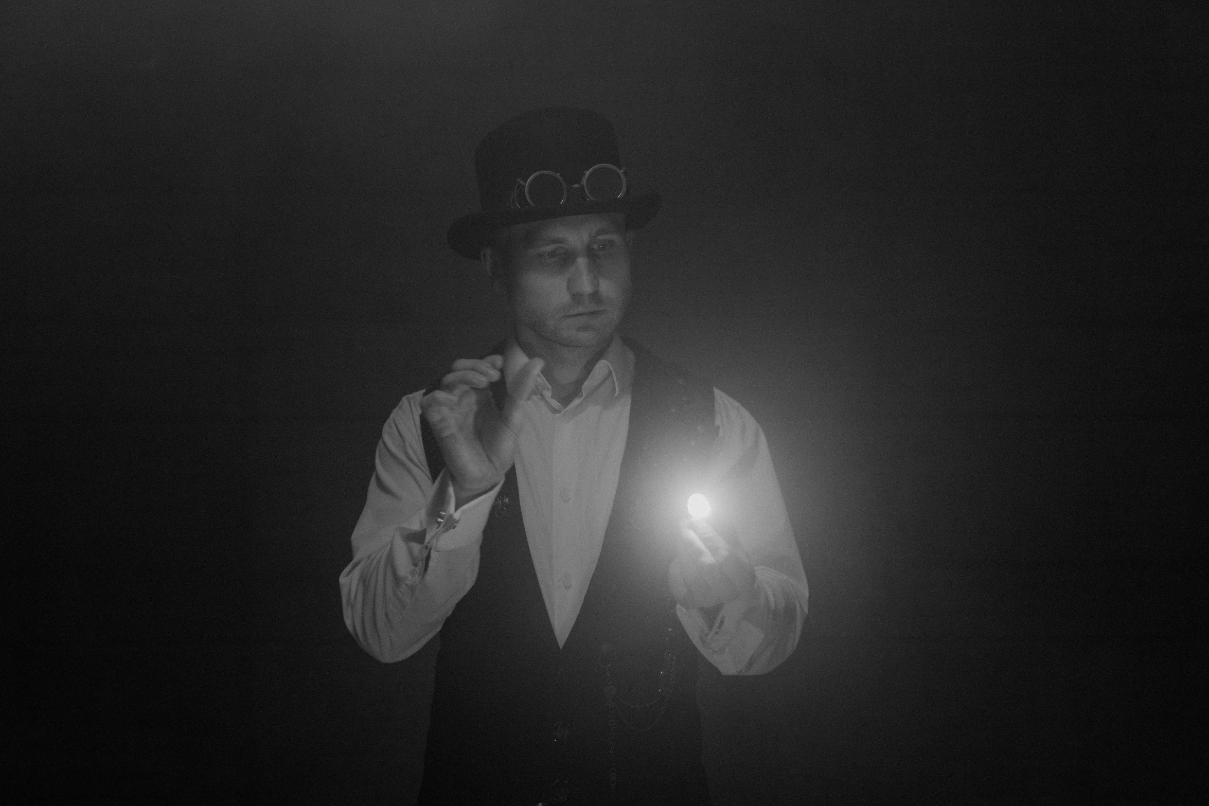 a black and white photo of a man holding a light, by Adam Marczyński, conceptual art, wearing steampunk top hat, hazy, sean harris wizard, with professional lighting